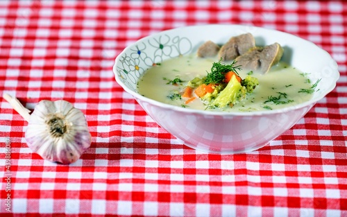 Green soup with meat  carrot  cream  garlic  broccoli and dill on a white plate on wooden background.