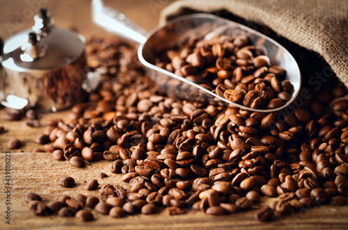 heap of roasted coffee beans with metal scoop on wooden table