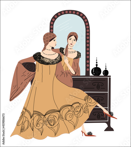 The woman is sitting at the dressing table. Retro fashion. Look in the dressing room mirror. Long dress with fur. Reflection in the mirror. The girl looks at herself. Graceful lady. Admire yourself.