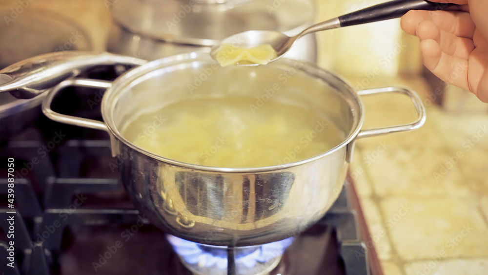 Italian pasta, farfalle, cooking in a pot full of boiling water; picking one with a spoon to check it.
Italian pasta, farfalle, cooking in a pot full of boiling water; picking one with a spoon to check it.