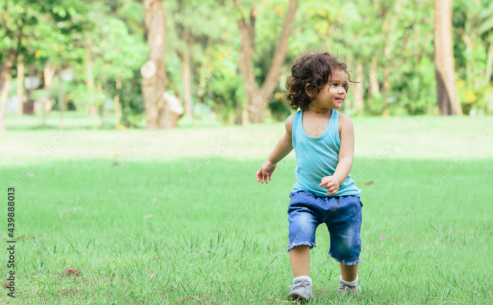 Little Caucasian little cute adorable curly hair playful girl wearing casual clothes, running alone with happiness and amusement in green garden or park or backyard during holidays. Little Caucasian little cute adorable curly hair playful girl wearing casual clothes, running alone with happiness and amusement in green garden or park or backyard during holidays.