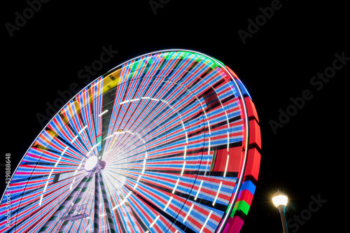 A night time carnival or state county fair ride  an eye or ferris wheel is lit up with neon LED lights as it spins  creation motion trails and sometimes motion sickness for riders aboard