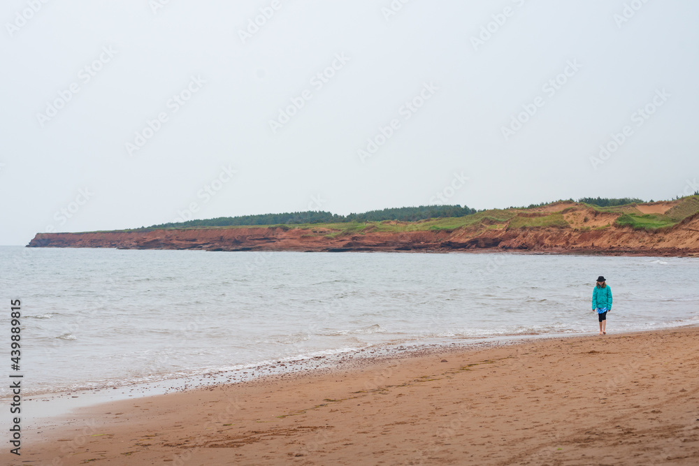 Girl Walking Barefoot along Sandy Red Beach on PEI on Overcast Rainy Day Girl Walking Barefoot along Sandy Red Beach on PEI on Overcast Rainy Day