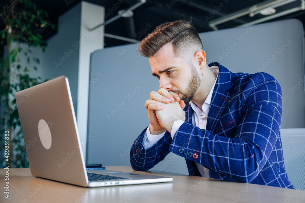 Thoughtful businessman in touching his chin, pondering ideas or strategy, sitting at his desk with a laptop, freelancer working on an online project, student preparing for the exam Thoughtful businessman in touching his chin, pondering ideas or strategy, sitting at his desk with a laptop, freelancer working on an online project, student preparing for the exam