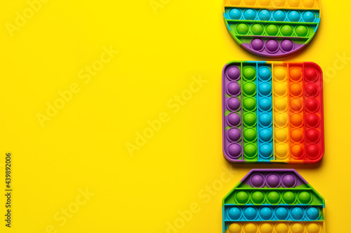 Rainbow pop it fidget toys on yellow background  flat lay. Space for text