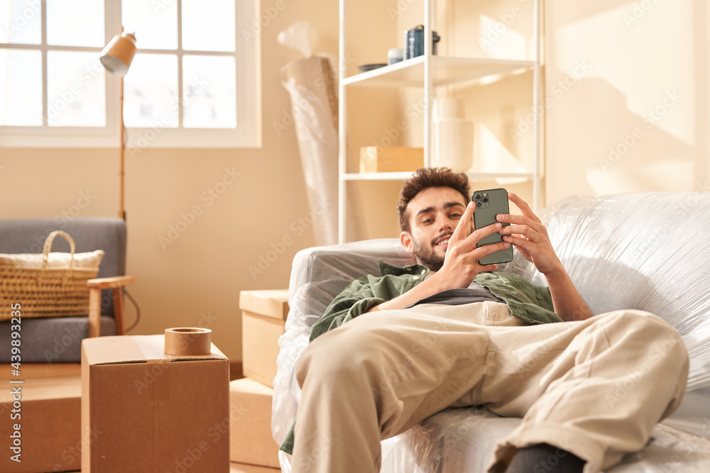 Relaxed male browsing smartphone on sofa during relocation Relaxed male browsing smartphone on sofa during relocation