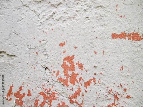 The red wall is painted with white paint. Over time, the top coat of paint has worn off. The texture is rough, many cracks and depressions. Copy space. 