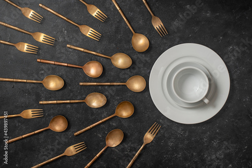 Fototapeta White ceramic plate, cup and brass forks and spoons look like sperm competition