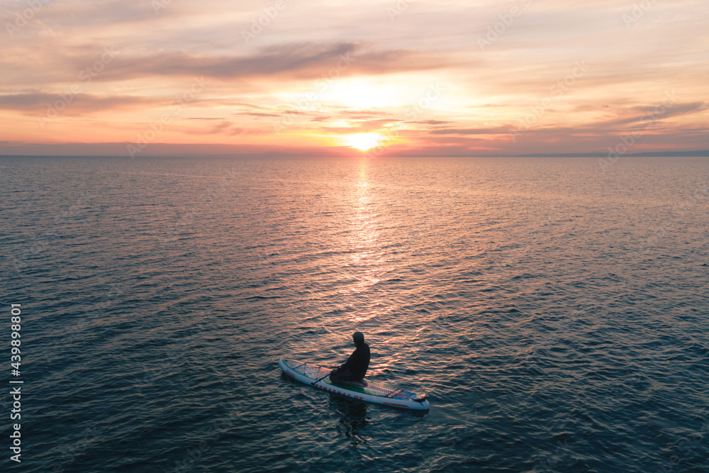 Fototapeta premium silhouette of a surfer in open water looking at the sun during a colorful sunset