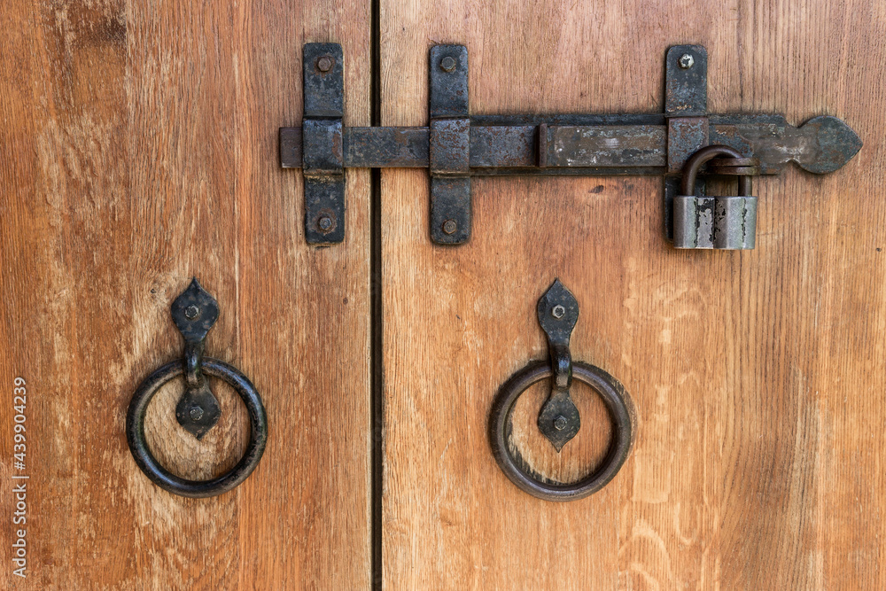Close-up of wooden doors with wrought iron handles and a deadbolt. Close-up of wooden doors with wrought iron handles and a deadbolt.
