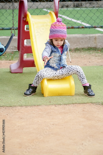 Criança linda brincando num parquinho de touca rosa e blusa azul no inverno depois da quarentena do covid 19. photo