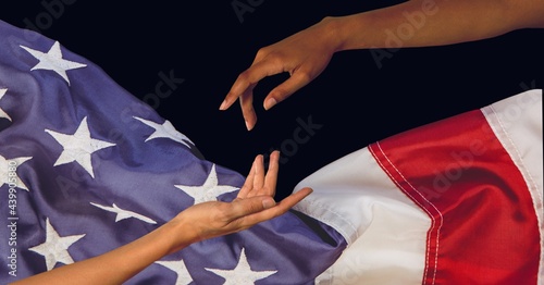 Composition of two diverse hands reaching above billowing american flag on black