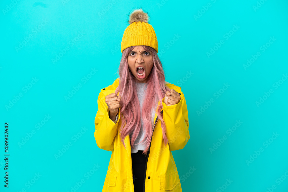 Young woman with pink hair wearing a rainproof coat isolated on blue background frustrated by a bad situation Young woman with pink hair wearing a rainproof coat isolated on blue background frustrated by a bad situation