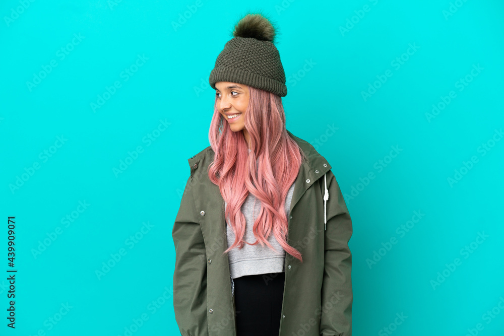 Young woman with pink hair wearing a rainproof coat isolated on blue background looking to the side and smiling Young woman with pink hair wearing a rainproof coat isolated on blue background looking to the side and smiling