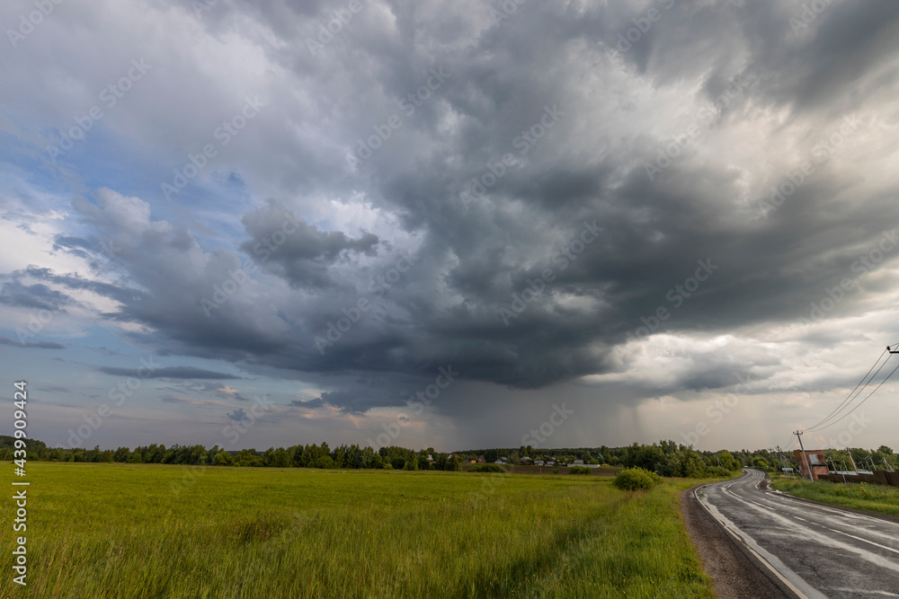 Rain clouds over the field. The road to the village. Green grass in the field. Summer landscape with storm clouds. Rain clouds over the field. The road to the village. Green grass in the field. Summer landscape with storm clouds.