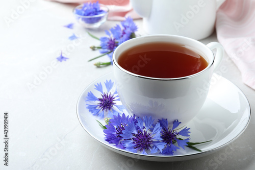 Cup of tea and cornflowers on light table, closeup. Space for text