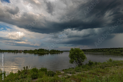 View of the lake from the old dam  overgrown with green grass. The water is brown with slight waves. Thick dark clouds before a storm on an evening summer day.