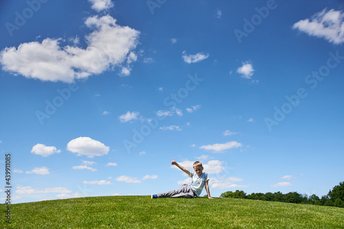 Boy 9 years old sits on a hill with green grass, summer