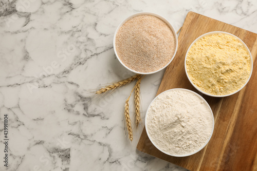 Different types of flours and wheat ears on white marble table, flat lay. Space for text