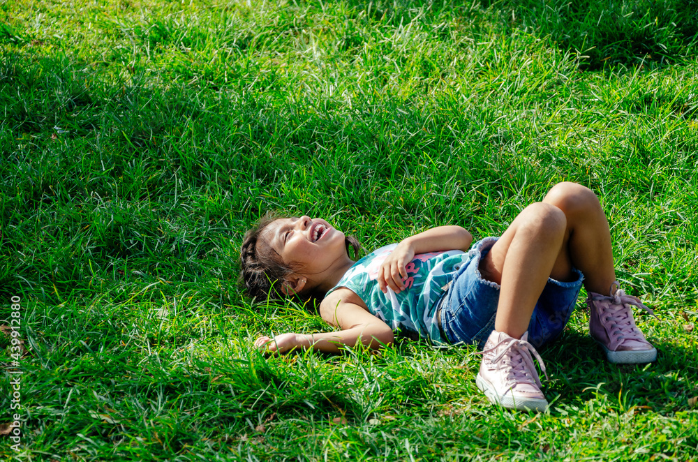 A little girl is smiling lying on the bright green grass. Portrait of a happy child on the grass in A little girl is smiling lying on the bright green grass. Portrait of a happy child on the grass in