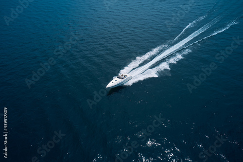 Large boat at high speed on dark blue water and top view. Boats top white waves on dark water. White boat top view. Aerial view of a boat in motion in dark water. © Berg