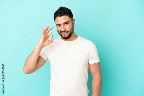 Young arab man isolated on blue background showing ok sign with fingers
