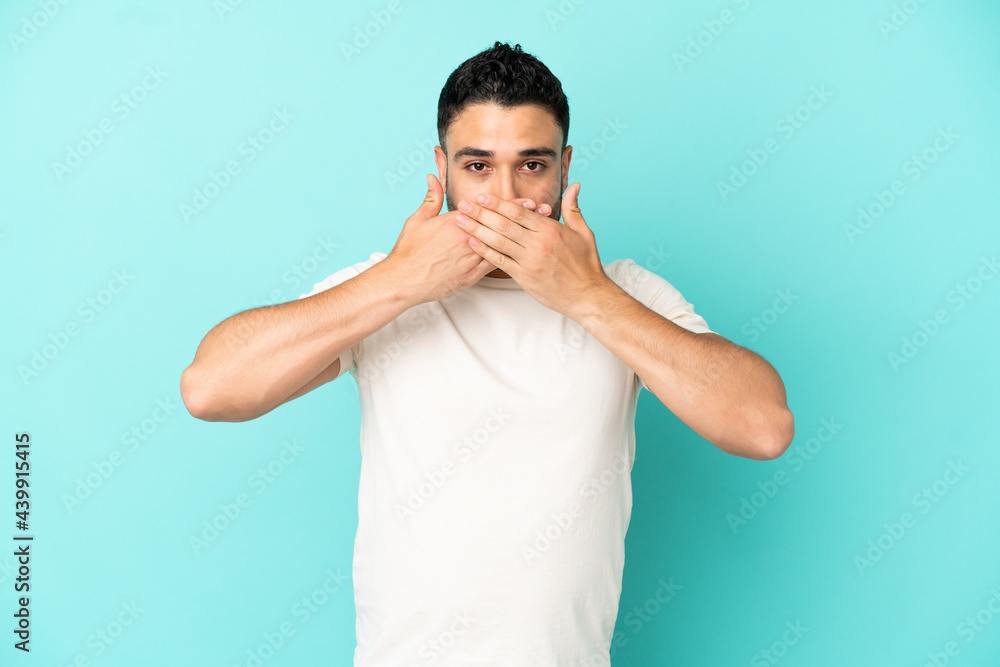 Young arab man isolated on blue background covering mouth with hands Young arab man isolated on blue background covering mouth with hands