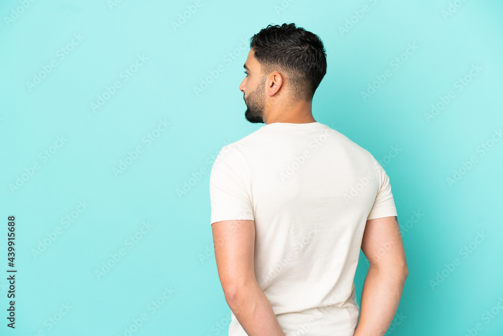 Young arab man isolated on blue background in back position and looking back Young arab man isolated on blue background in back position and looking back