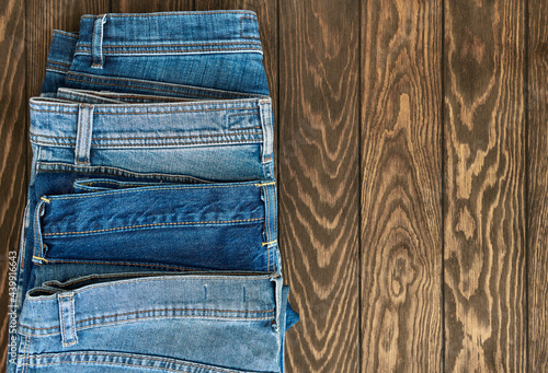 Vertical row of fashionable different jeans on a wooden background with copy space