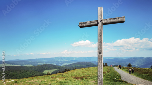 Wonderful view from Belchen hill mountain, surrounded by green fresh meadow, forest trees, wooden cross and people who hike - Landscape Southern Black Forest Aitern Germany background panorama