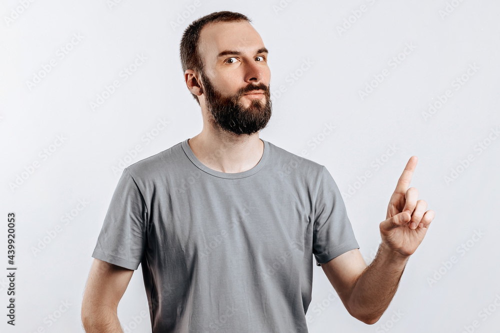 Portrait of cheerful young handsome man smiling looking at camera pointing finger upwards on white background with space for advertising mock up Portrait of cheerful young handsome man smiling looking at camera pointing finger upwards on white background with space for advertising mock up