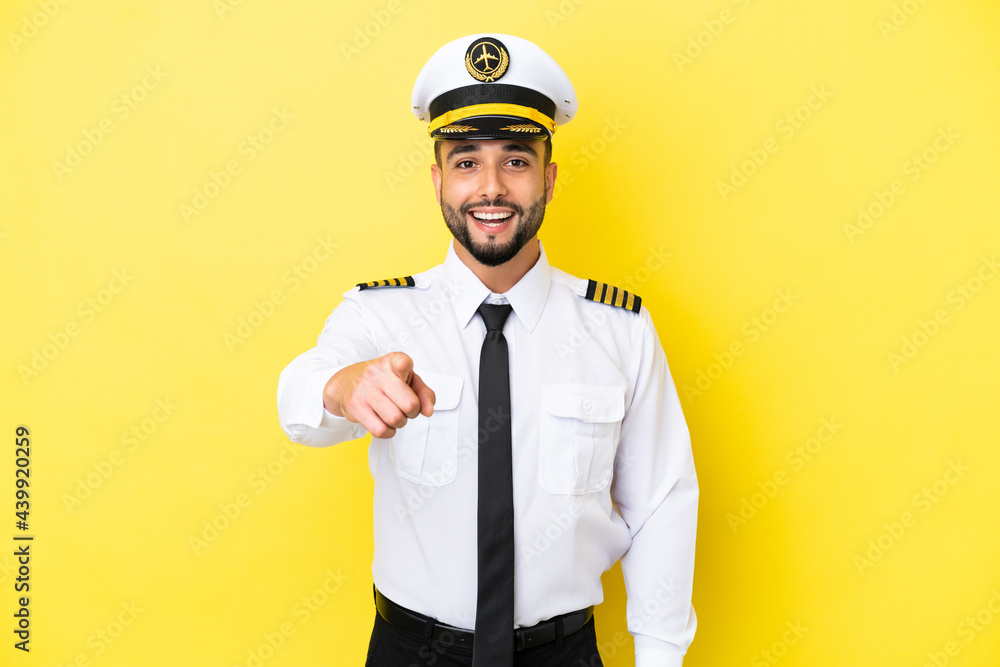 Airplane arab pilot man isolated on yellow background surprised and pointing front Airplane arab pilot man isolated on yellow background surprised and pointing front