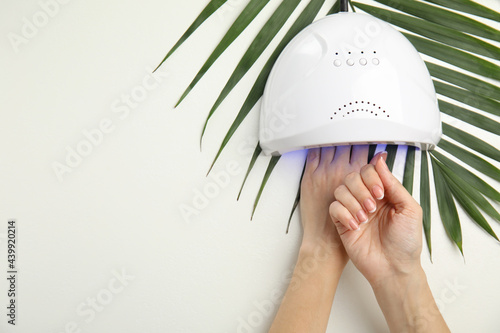 Woman using ultraviolet lamp to dry gel nail polish on white background, top view. Space for text