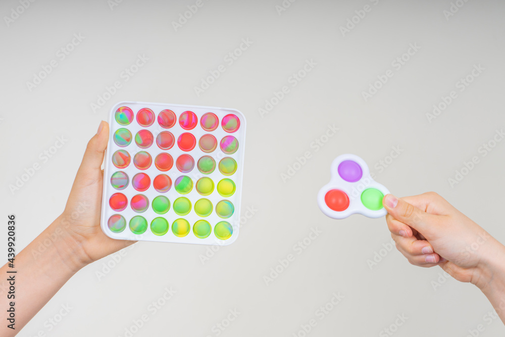 Kids hands holding pop it fidget toys. Push pop-it fidgeting game helps relieve stress, anxiety, autism, provide sensory and tactile experience for children Kids hands holding pop it fidget toys. Push pop-it fidgeting game helps relieve stress, anxiety, autism, provide sensory and tactile experience for children