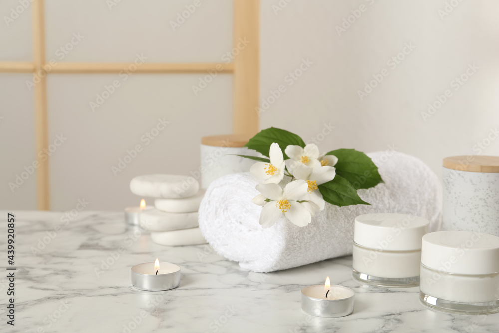 Composition with beautiful jasmine flowers and skin care products on white marble table indoors, space for text