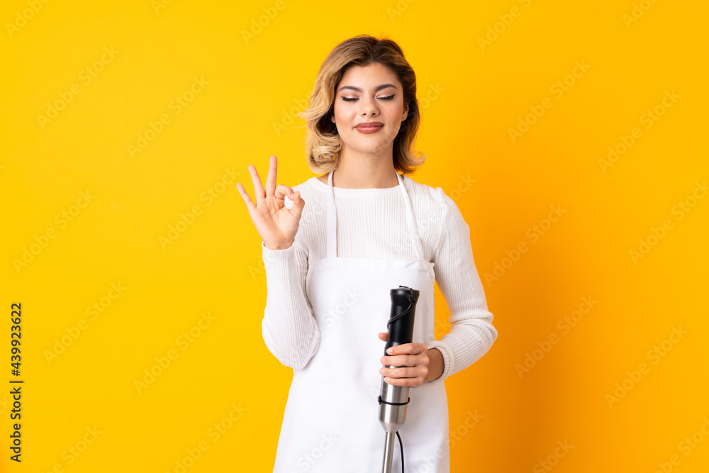Girl using hand blender isolated on yellow background in zen pose Girl using hand blender isolated on yellow background in zen pose