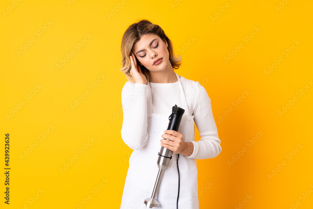 Girl using hand blender isolated on yellow background with headache