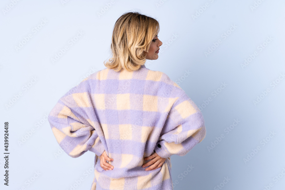 Young Russian woman isolated on blue background in back position and looking side Young Russian woman isolated on blue background in back position and looking side