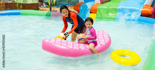 Happy young little kid girl with a pink inflatable with mother at the outdoor swimming pool on summer sunny day