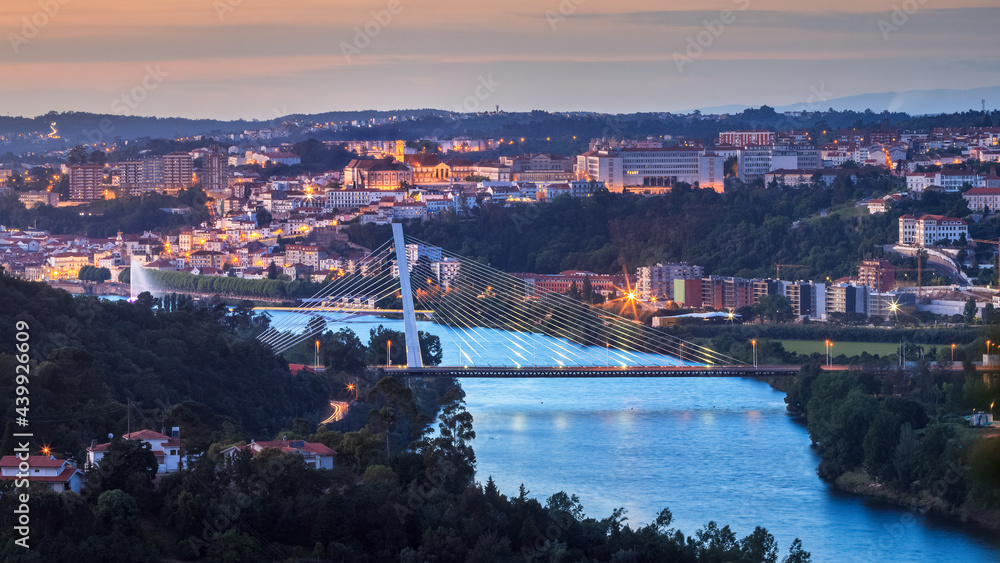 Fototapeta premium Panoramic view of Coimbra at dusk, in Portugal, with the Mondego river and the Rainha Santa Isabel bridge in the foreground and the university with its tower in the background.