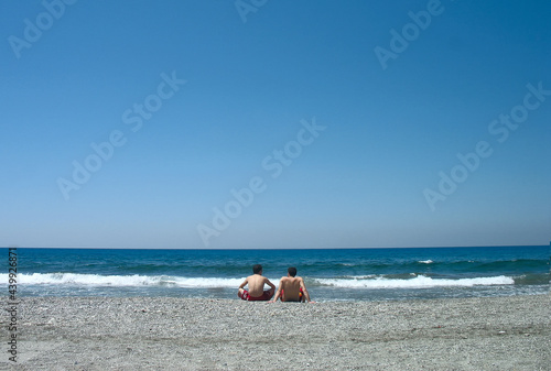 travel photography, two young guys are sitting on the seashore rear view on blue sky background closeup. Selective focus