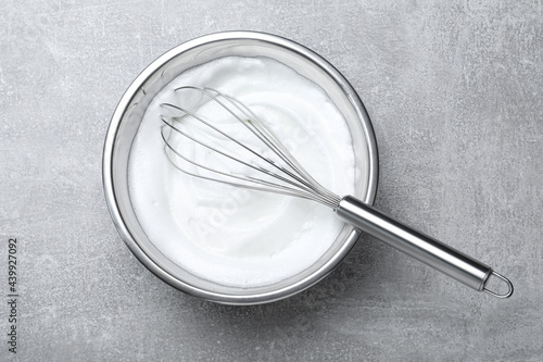 Obraz na plátne Whipped egg whites with balloon whisk on grey table, top view