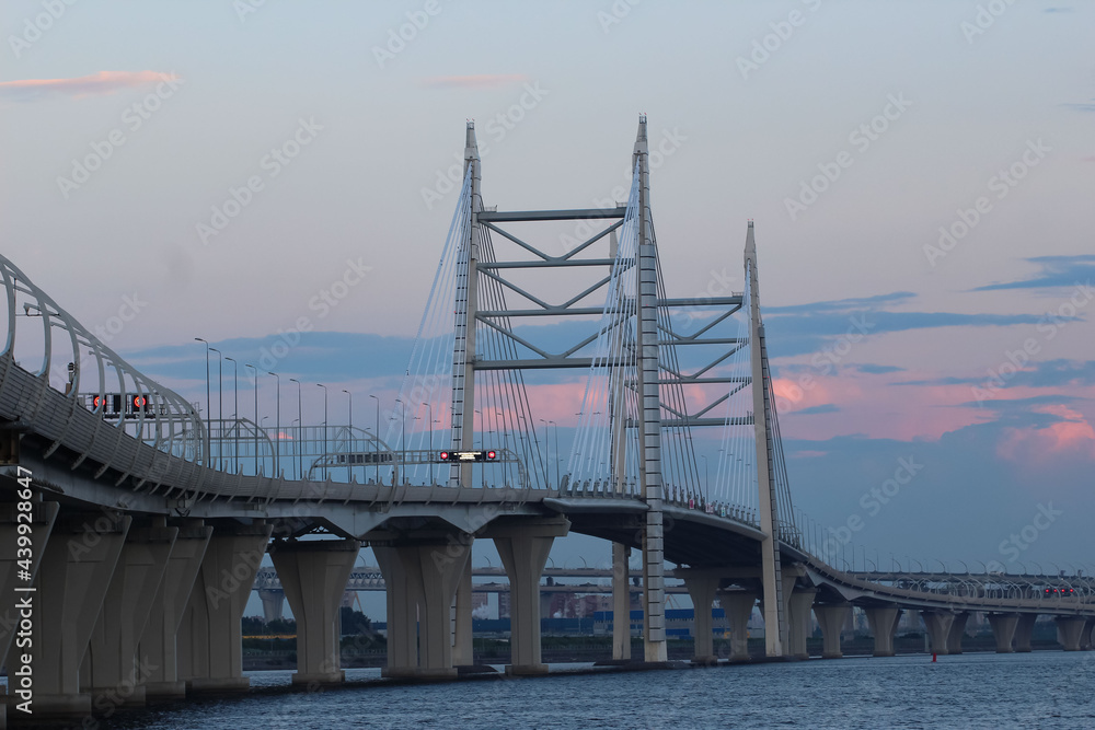 Fototapeta premium Close-up of the cable bridge and the motorway over the bay against the evening sky with red reflexes from the setting sun, 