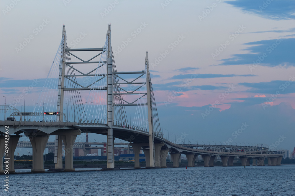 Close-up of the cable bridge and the motorway over the bay against the evening sky with red reflexes from the setting sun, 