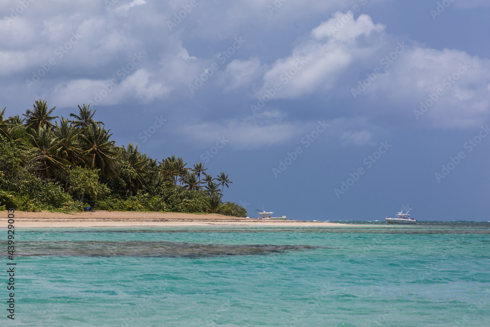 Fototapeta premium Dramatic image of the Caribbean coast with turquoise blue water in foreground and palms on the coast with fishing boats in the background.
