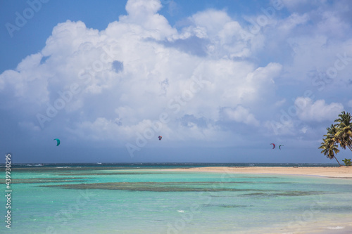 Dramatic image of parasailing on the Caribbean coast with turquoise blue water and cloudy skies and palm trees.