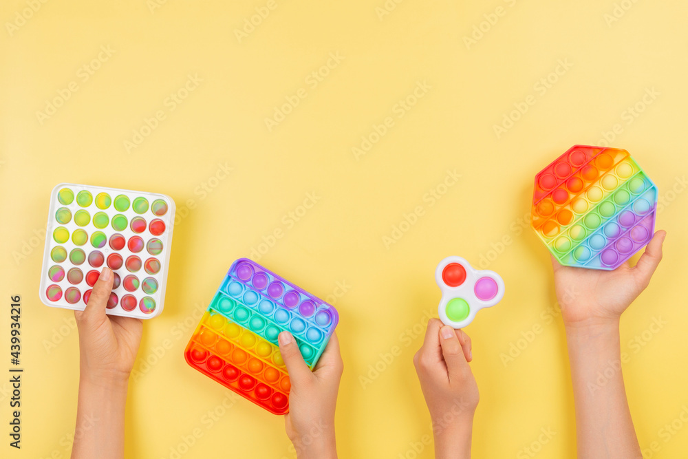 Many hands holding colorful pop it fidget toys on yellow background. Push pop-it fidgeting game helps relieve stress, anxiety, autism, provide sensory and tactile experience for children Many hands holding colorful pop it fidget toys on yellow background. Push pop-it fidgeting game helps relieve stress, anxiety, autism, provide sensory and tactile experience for children