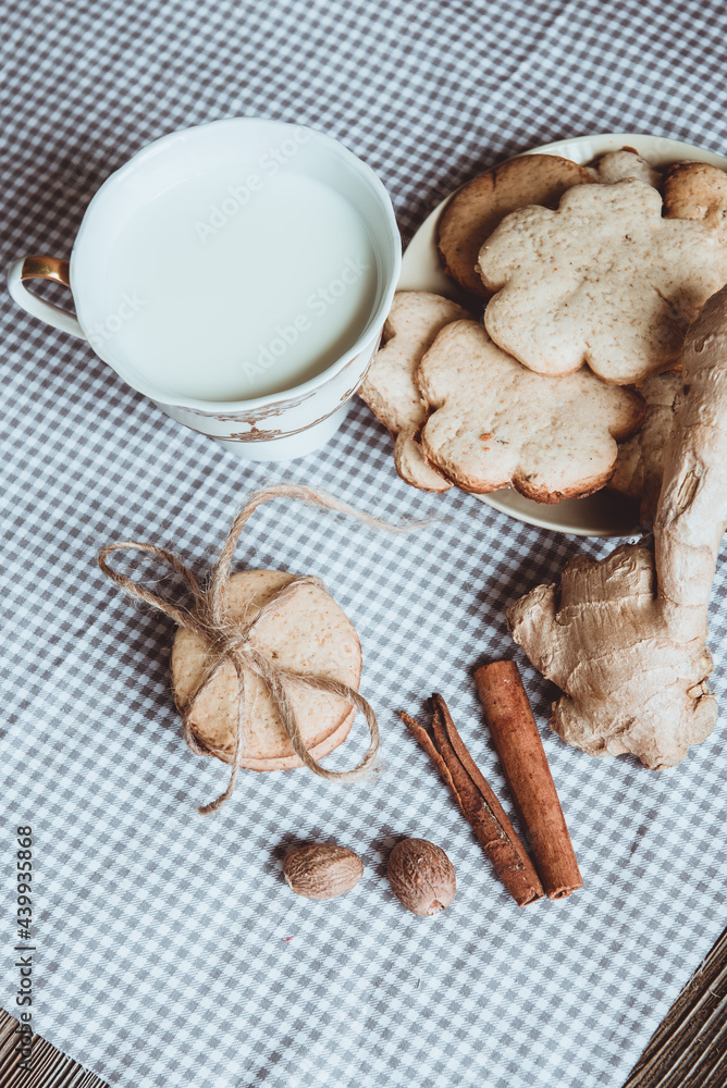 Close up of homemade ginger cookies, cinnamon, ginger with cup of milk on a towel wooden table. Copy space. Retro toned image, flat lay Close up of homemade ginger cookies, cinnamon, ginger with cup of milk on a towel wooden table. Copy space. Retro toned image, flat lay