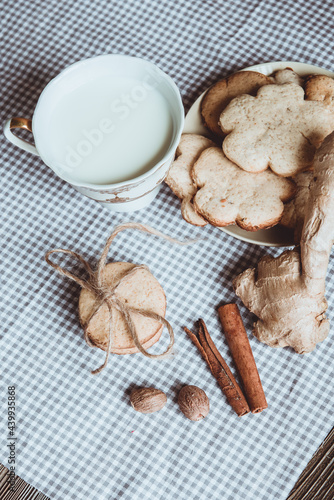 Close up of homemade ginger cookies, cinnamon, ginger with cup of milk on a towel wooden table. Copy space. Retro toned image, flat lay