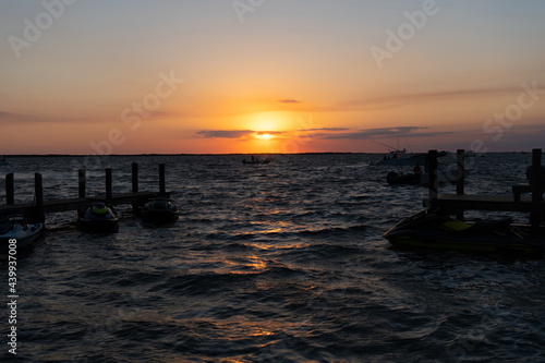 romantic sundown seascape with silhouette pier jet ski and yacht boats, summer vacation.